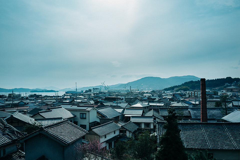 The Akitsu-cho area where Imada Sake Brewing Co., Ltd. is located. It is a small port town facing the Seto Inland Sea. In the 19th century, brewers from this area established a method of producing sake with soft water, which had until then been considered ill-suited to the task. The pioneering spirit and technical skills of craftsmen who created new approaches in the face of adversity, as well as the sophisticated palates of the inhabitants of Akitsu-cho developed by the abundant natural bounty of the local seas and mountains, have improved the flavor of the town’s sake. MAE KOSUKE 