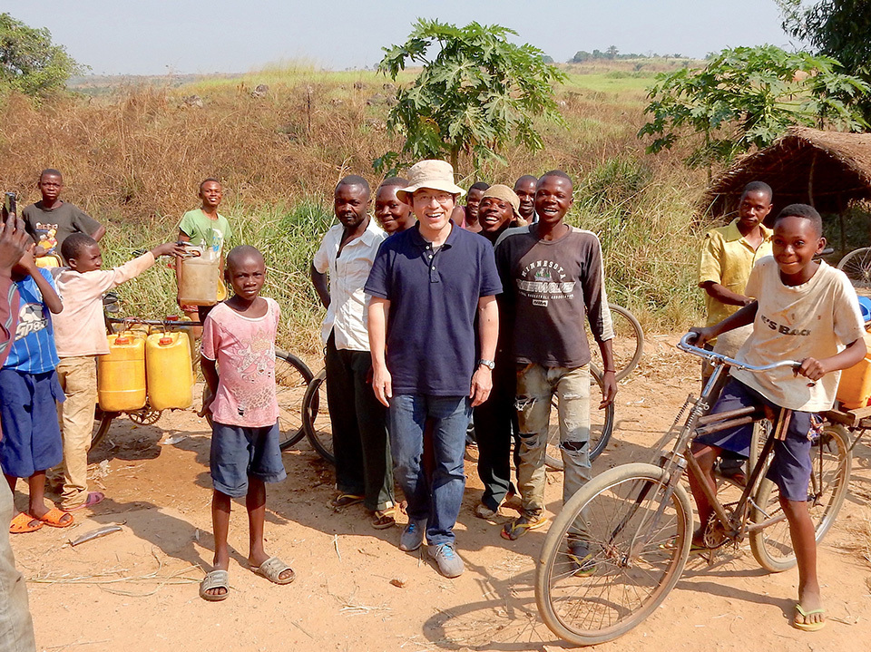 Professor KANEKO Satoshi stands smiling surrounded by African children.