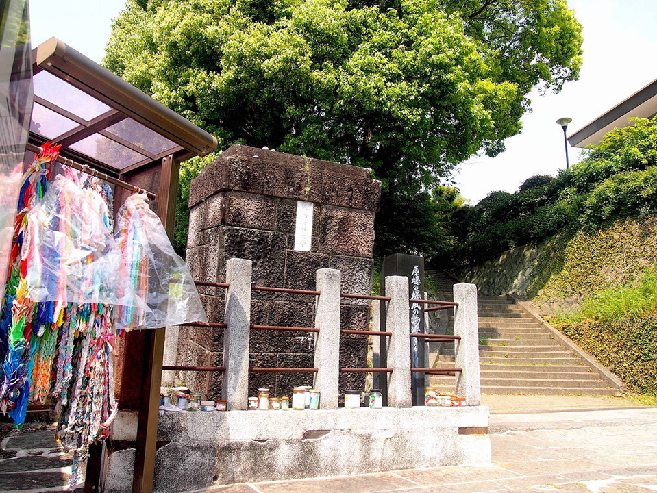 An old gatepost scorched by the atomic bombing. Beside it, a thousand paper cranes are displayed.