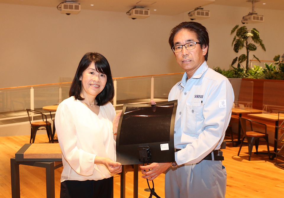A man and woman standing next to each other and holding a film-like solar cell.
