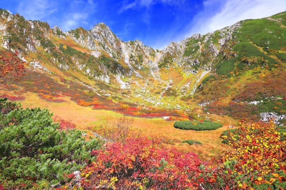 Senjojiki Cirque in autumn, vibrant fall colors with red and yellow foliage, rugged mountain peaks, and clear blue sky