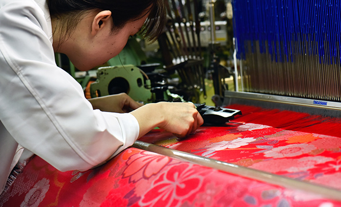 A person working on a large piece of vibrant red and pink Nishijin fabric.