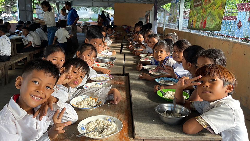 Children enjoying lunch together at a school cafeteria, sharing smiles and food in a lively atmosphere.