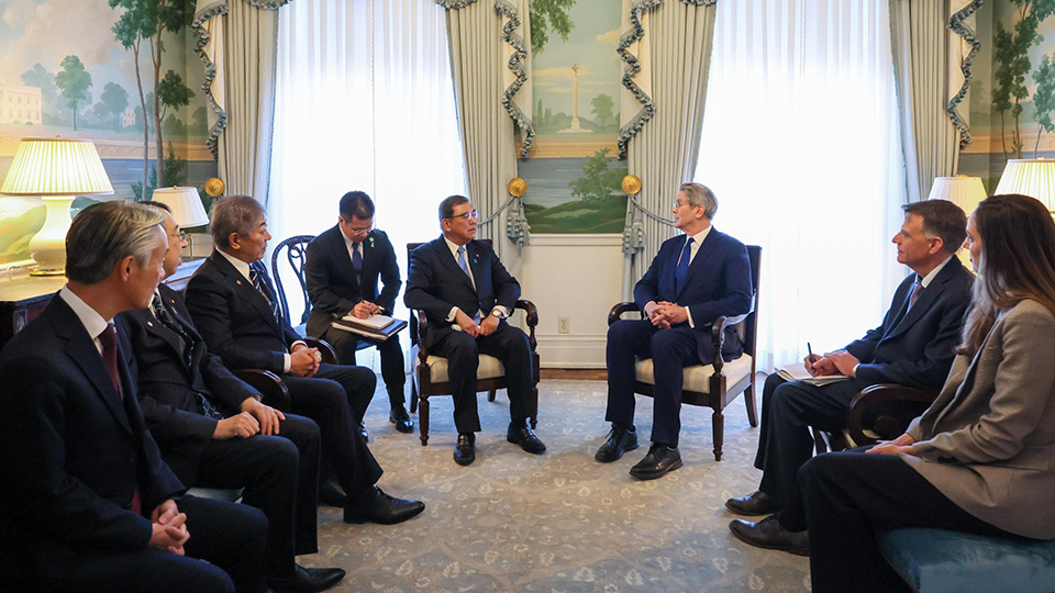 A diverse group of individuals engaged in conversation, seated around the walls in a bright and inviting indoor space.
