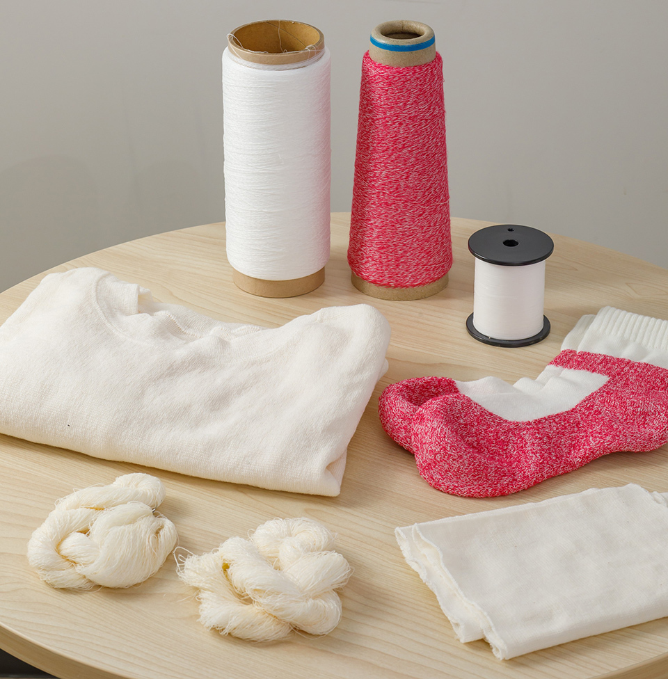 Spools of thread (white and red) with fabric swatches and prototype clothing items made with Craze-tex displayed on a round wooden table.