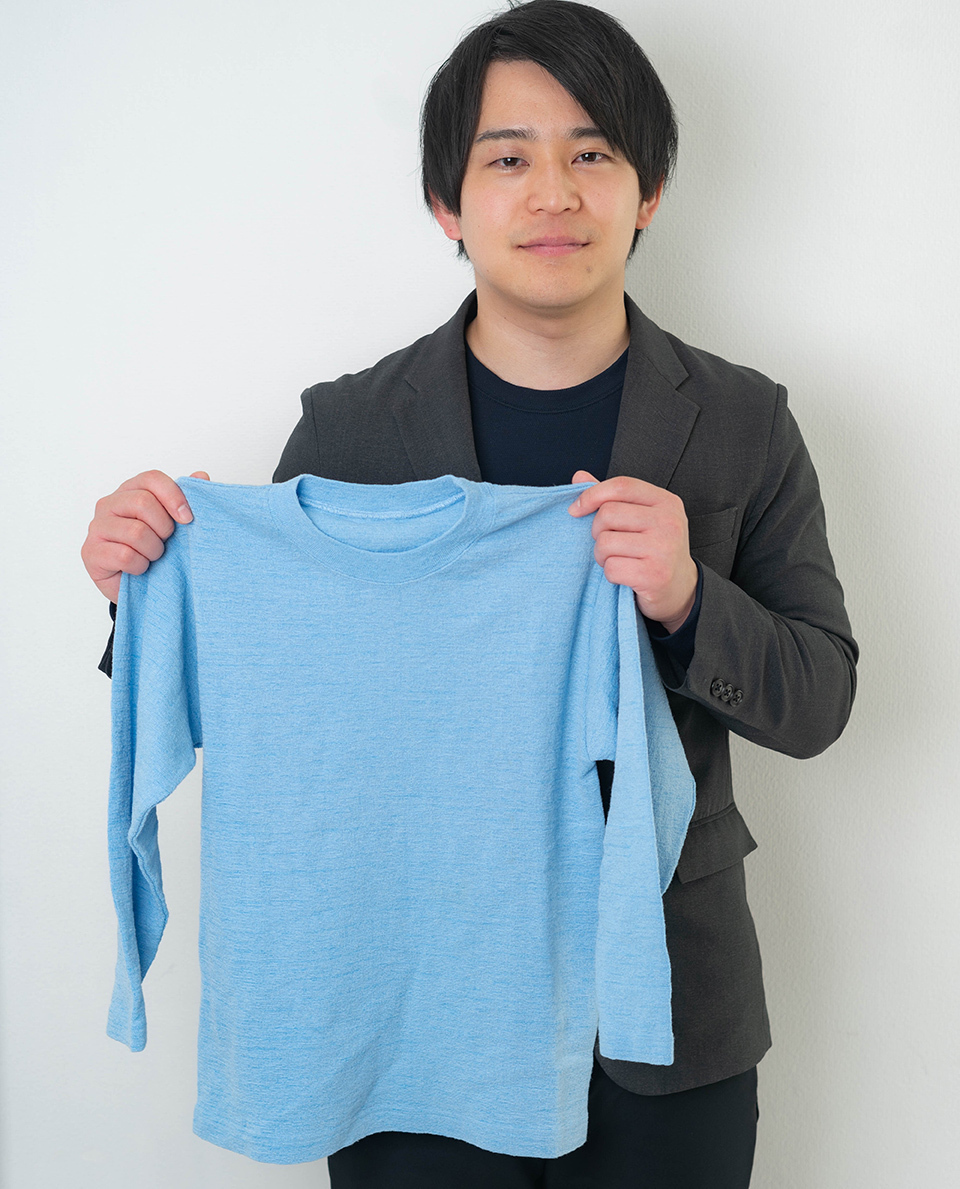 CHOSOKABE Shunya, president and representative director of FiberCraze Corporation, proudly displays a blue long-sleeved T-shirt made with Craze-tex.