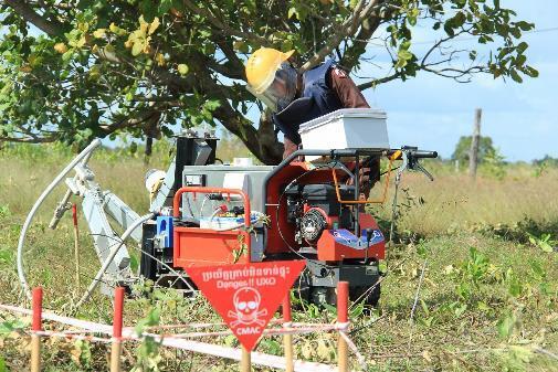 A man in a yellow helmet operates a machine, part of a mine-clearing robot project in Cambodia.