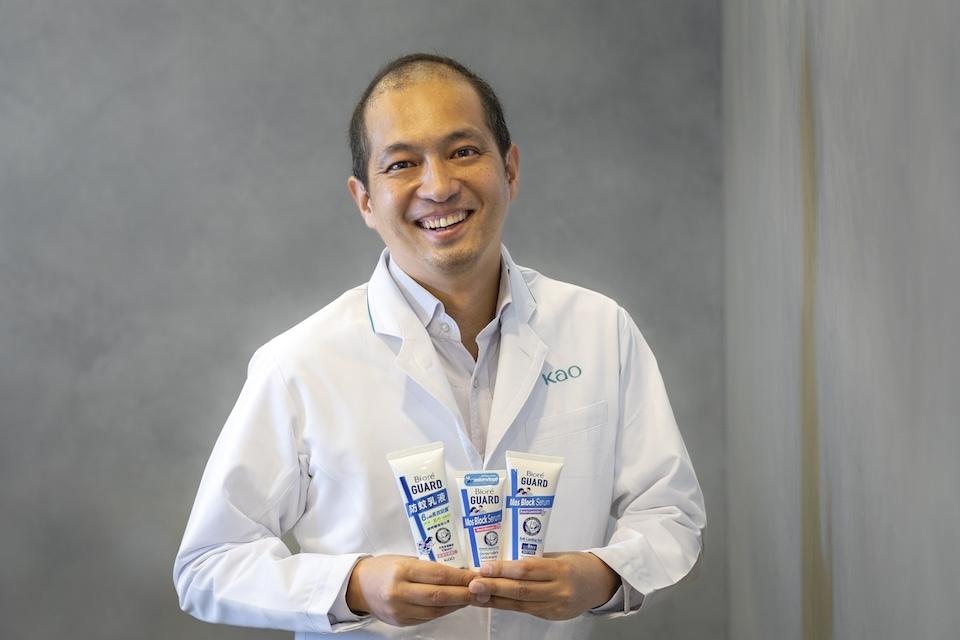 A smiling man in a white coat holds three bottles of repellent cream.