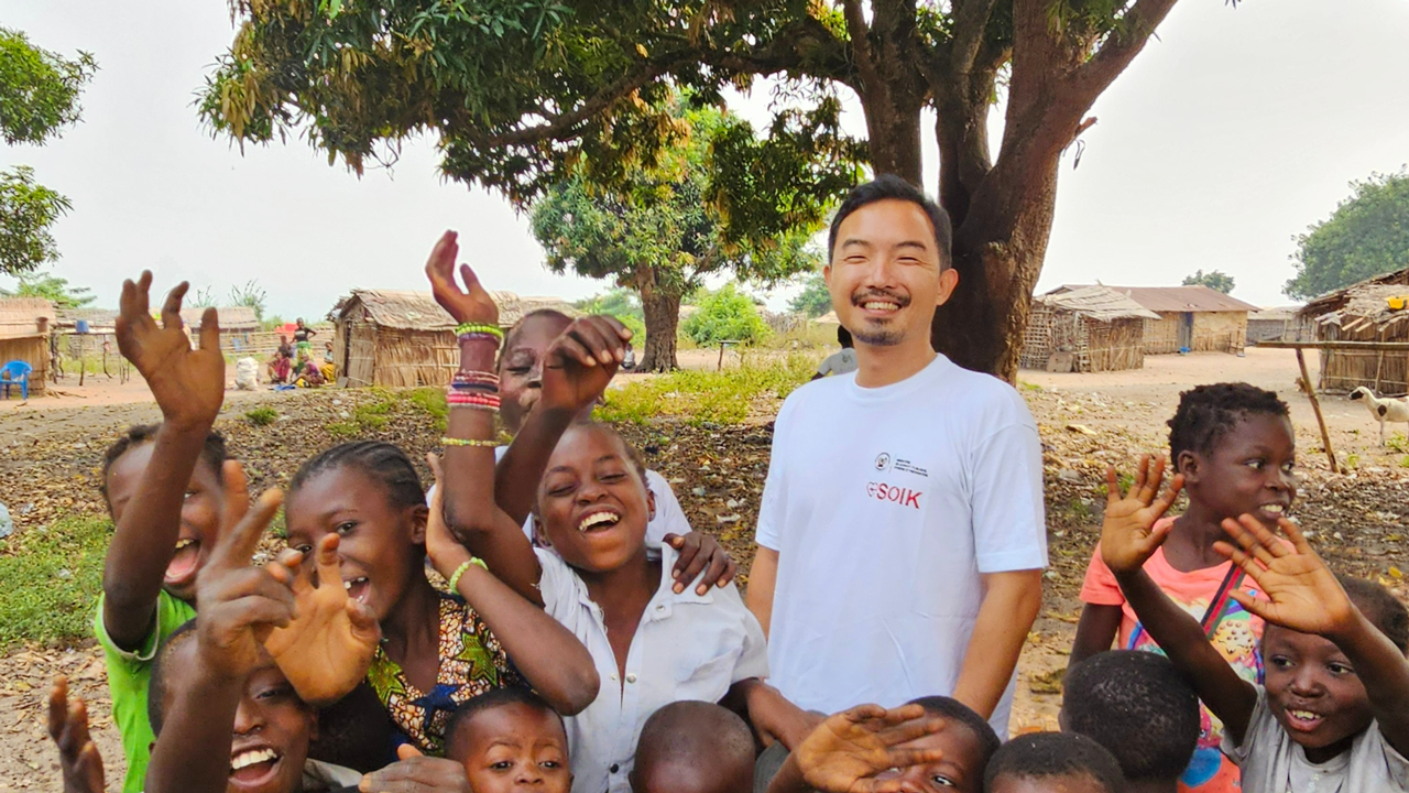 A Japanese man surrounded by excited kids in Africa