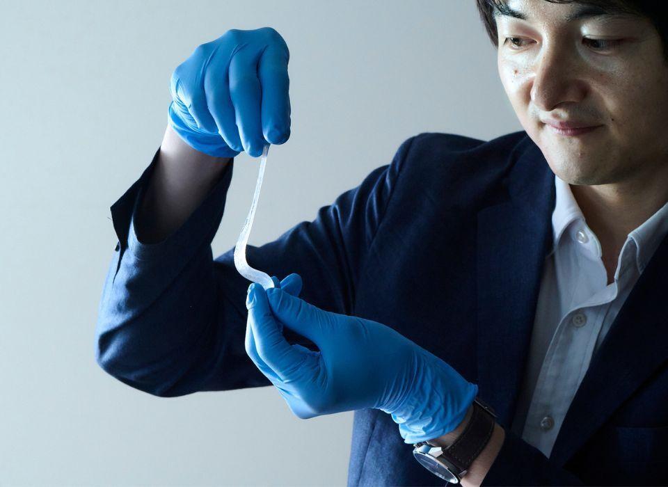 A man in a suit jacket and blue latex gloves manipulating a piece of white gel
