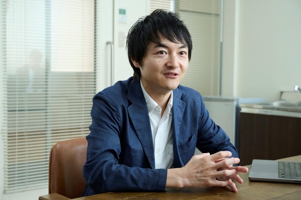 A photo of Masui Kosuke, a Japanese man wearing a blue jacket and sitting at a desk