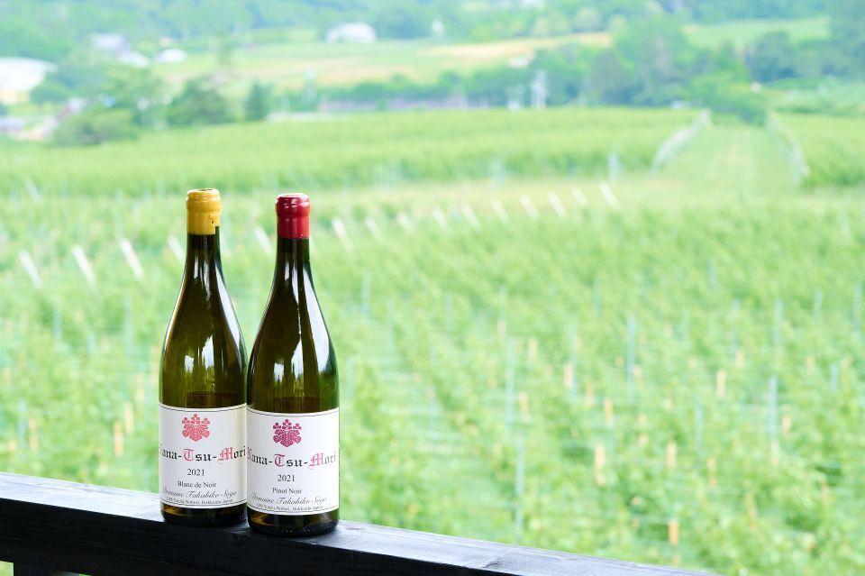 A photo of two wine bottles against a backdrop of a green vineyard