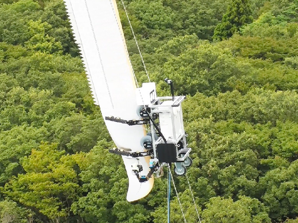 Photo of a robot on the tip of a wind turbine blade, high above a forest