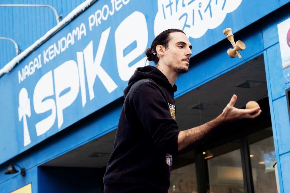 Shelby Brown demonstrating a kendama trick in front of the blue SPIKe frontage