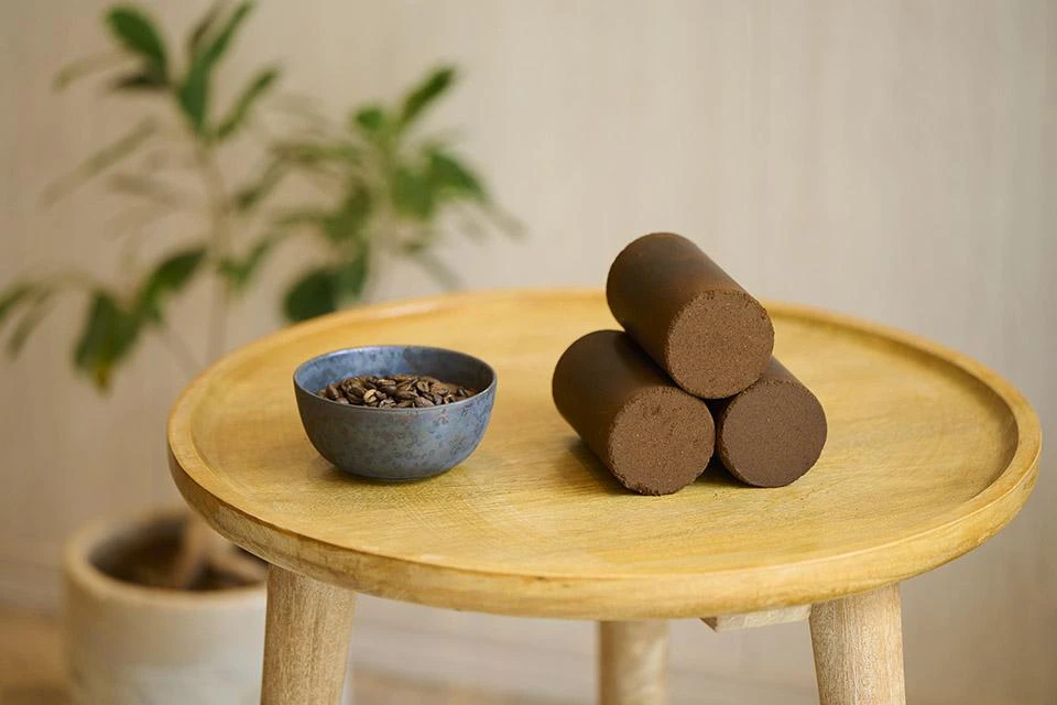 A bowl of coffee next to coffee grounds molded into solid pellets, placed on a small wooden table