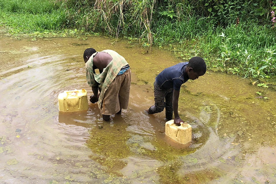 Two people filling up large canisters with water in a small pond 